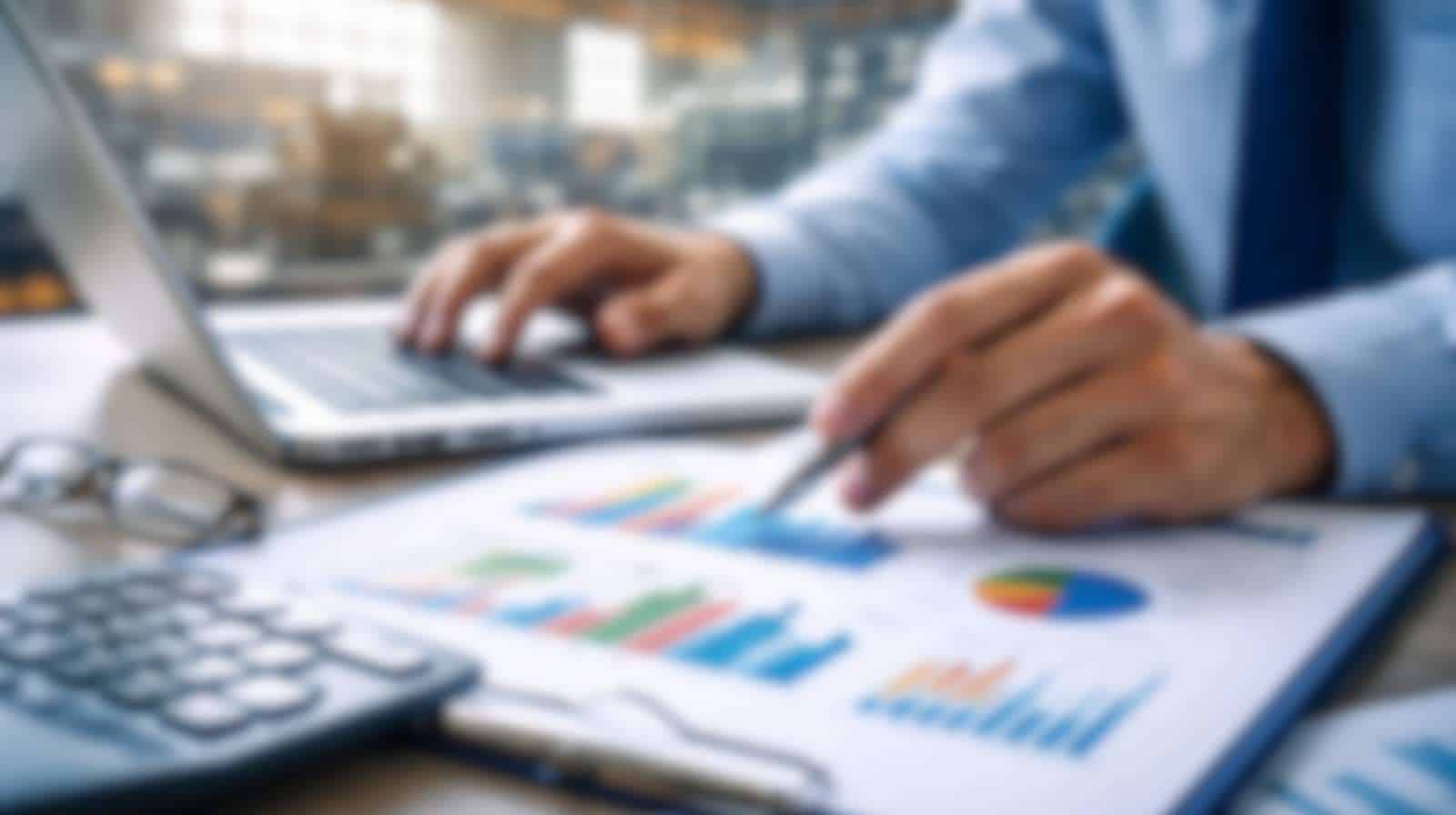 Analista econômico revisando relatórios industriais em laptop com gráficos financeiros, representando a análise do IPP na indústria.