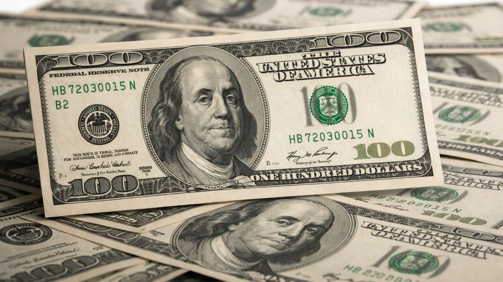 Nota de 100 dólares em close sobre outras cédulas, destacando o dólar em alta no mercado financeiro.