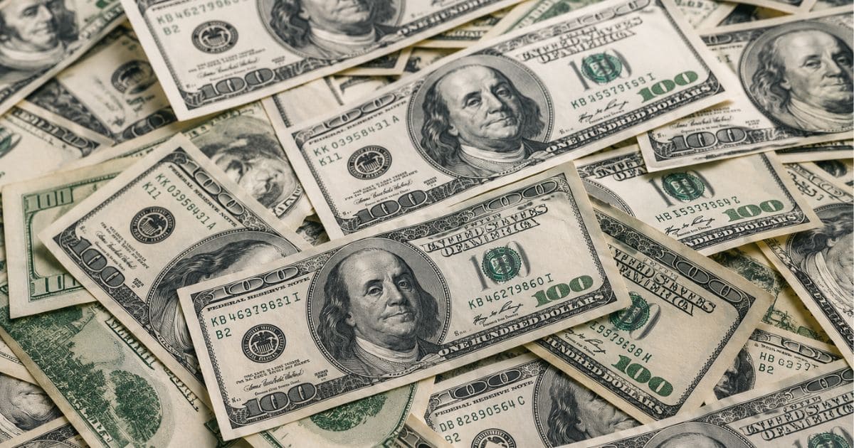 Montanha de notas de 100 dólares espalhadas e sobrepostas, destacando o rosto de Benjamin Franklin em várias cédulas, em uma composição que remete ao mercado financeiro, câmbio e fluxo internacional de capital.