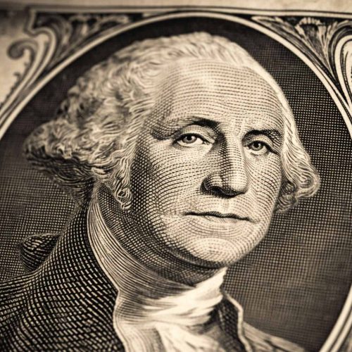 Close-up de uma nota de um dólar americano, com foco no retrato de George Washington, mostrando detalhes das linhas e da textura do papel-moeda.