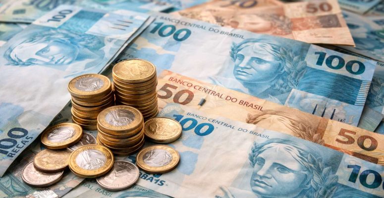 Notas e moedas de real brasileiro espalhadas sobre uma mesa, com destaque para cédulas de 100 e 50 reais e moedas empilhadas.