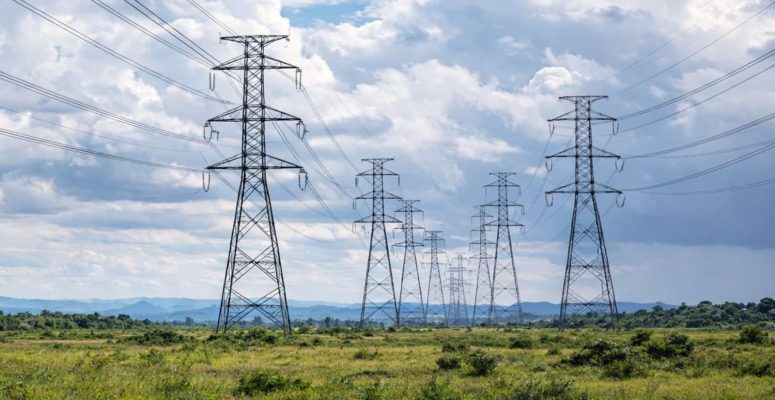 Linhas de transmissão de energia em longa distância atravessando área rural sob céu parcialmente nublado, representando infraestrutura do setor elétrico.