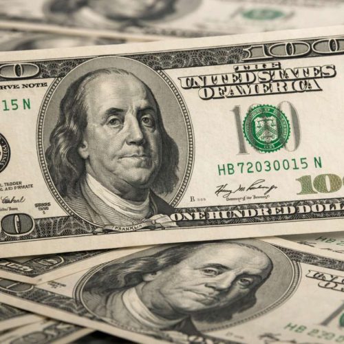 Nota de 100 dólares em close sobre outras cédulas, destacando o dólar em alta no mercado financeiro.