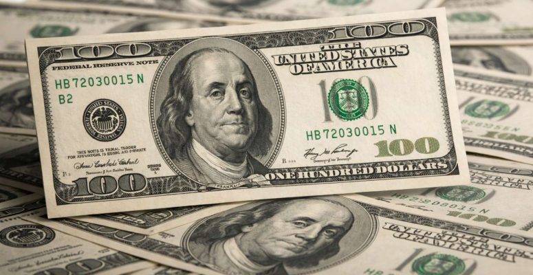 Nota de 100 dólares em close sobre outras cédulas, destacando o dólar em alta no mercado financeiro.