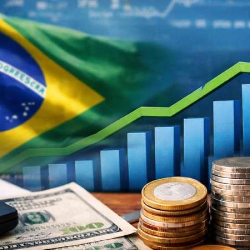 Ilustração com pilhas de moedas, calculadora e bandeira do Brasil ao fundo, representando o cenário econômico e as finanças públicas do país.