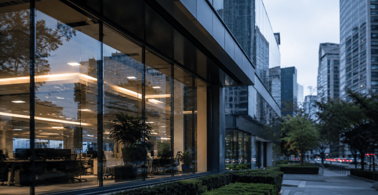 Prédio corporativo moderno com fachada de vidro iluminada ao entardecer em centro financeiro urbano, representando ambiente do mercado financeiro e setor bancário.