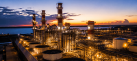 Refinaria e complexo termelétrico da Eneva iluminados ao entardecer, com estruturas industriais, tanques de gás natural e torres de geração de energia em destaque.