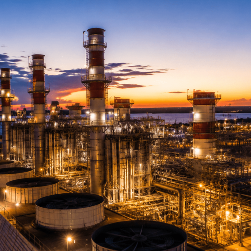 Refinaria e complexo termelétrico da Eneva iluminados ao entardecer, com estruturas industriais, tanques de gás natural e torres de geração de energia em destaque.