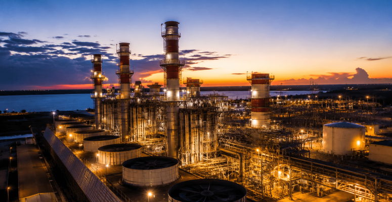 Refinaria e complexo termelétrico da Eneva iluminados ao entardecer, com estruturas industriais, tanques de gás natural e torres de geração de energia em destaque.