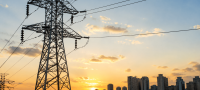 Torres de transmissão de energia elétrica ao pôr do sol com skyline urbano ao fundo, representando o setor elétrico e infraestrutura da Equatorial.