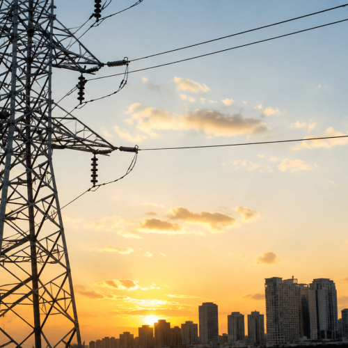 Torres de transmissão de energia elétrica ao pôr do sol com skyline urbano ao fundo, representando o setor elétrico e infraestrutura da Equatorial.