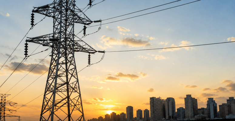 Torres de transmissão de energia elétrica ao pôr do sol com skyline urbano ao fundo, representando o setor elétrico e infraestrutura da Equatorial.